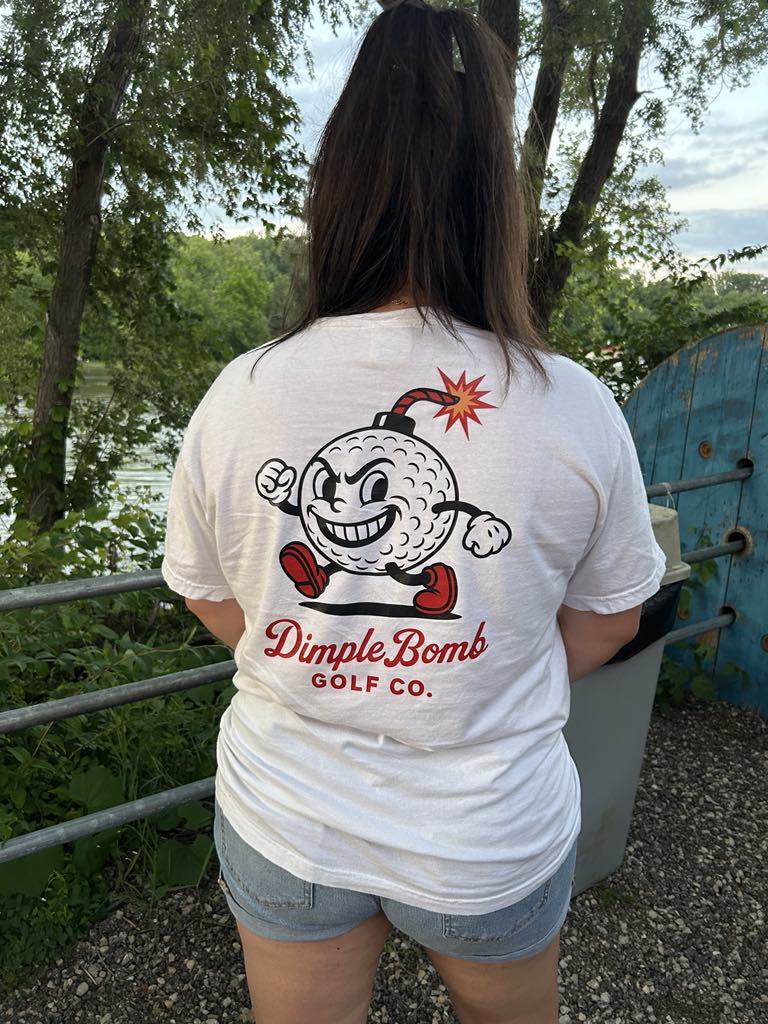 Person wearing Dimple Bomb white t-shirt with a graphic design and text outdoors.