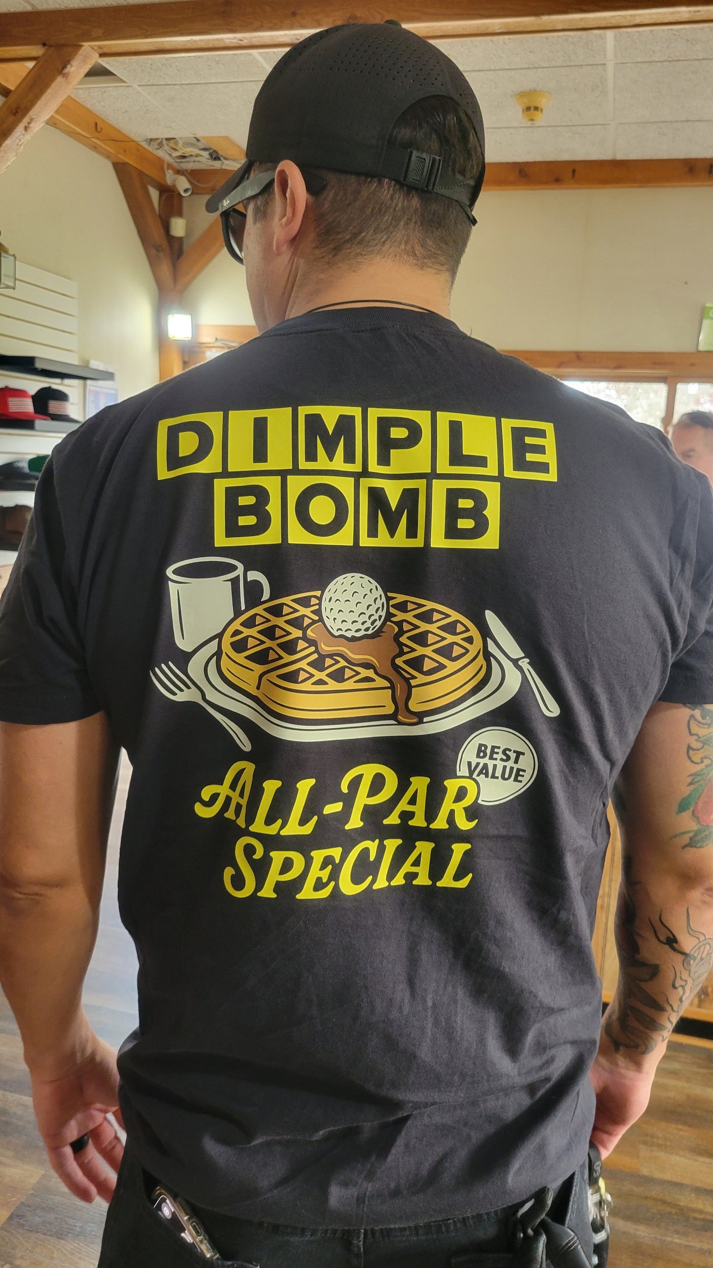 Person wearing a black t-shirt with a graphic and text on the back, standing indoors.