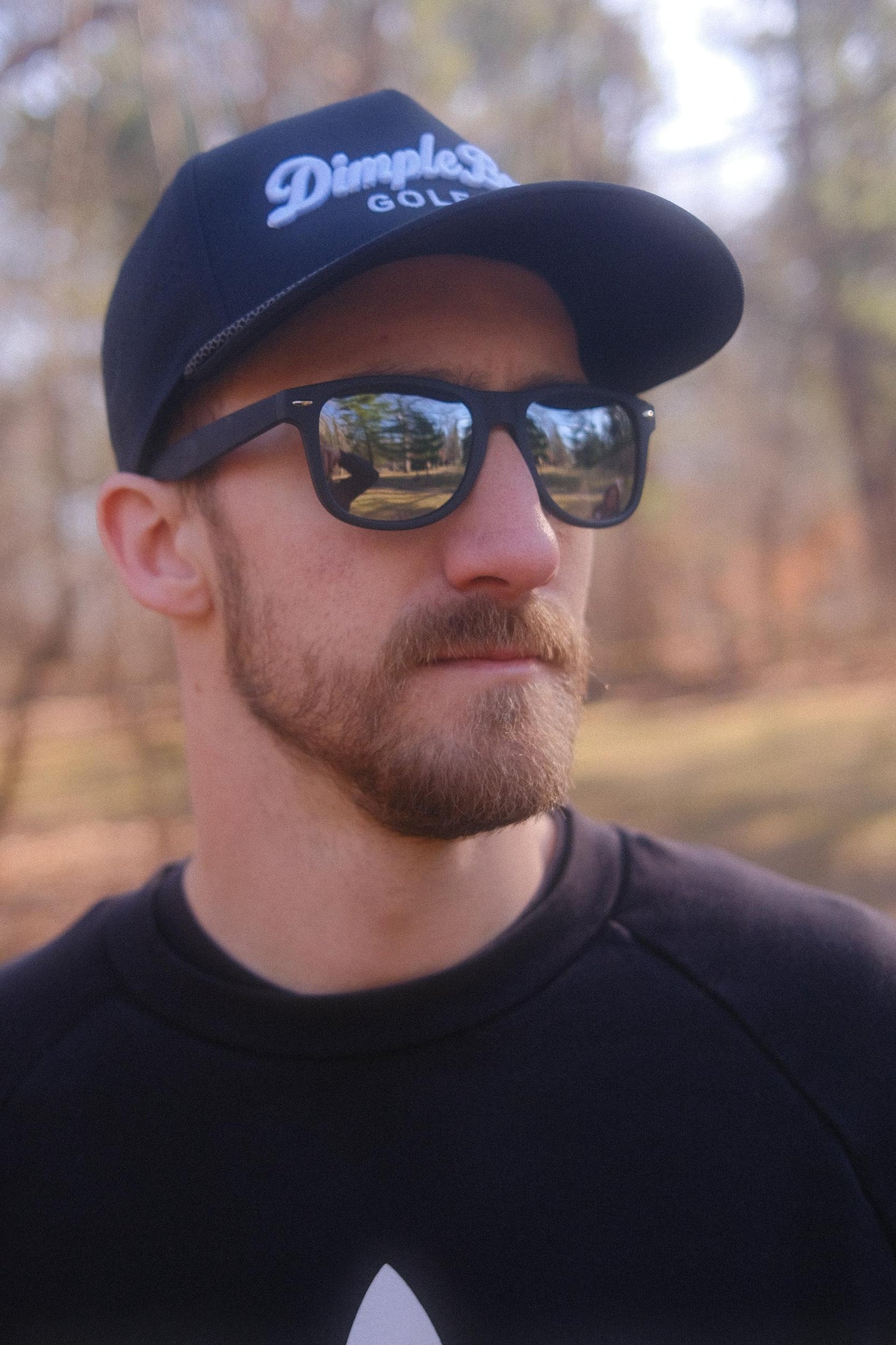 Man wearing a black cap and sunglasses with a blurred natural background